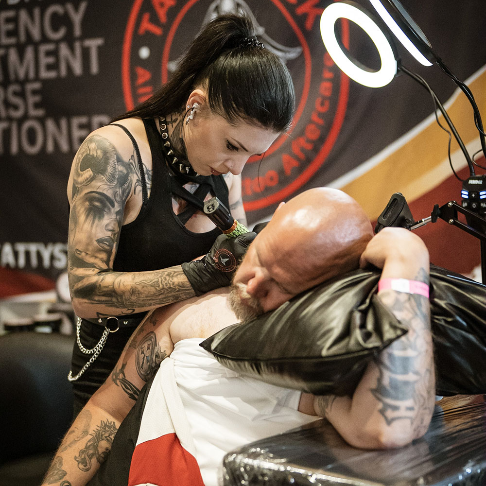 Man being tattooed by female artist while holding a pillow 