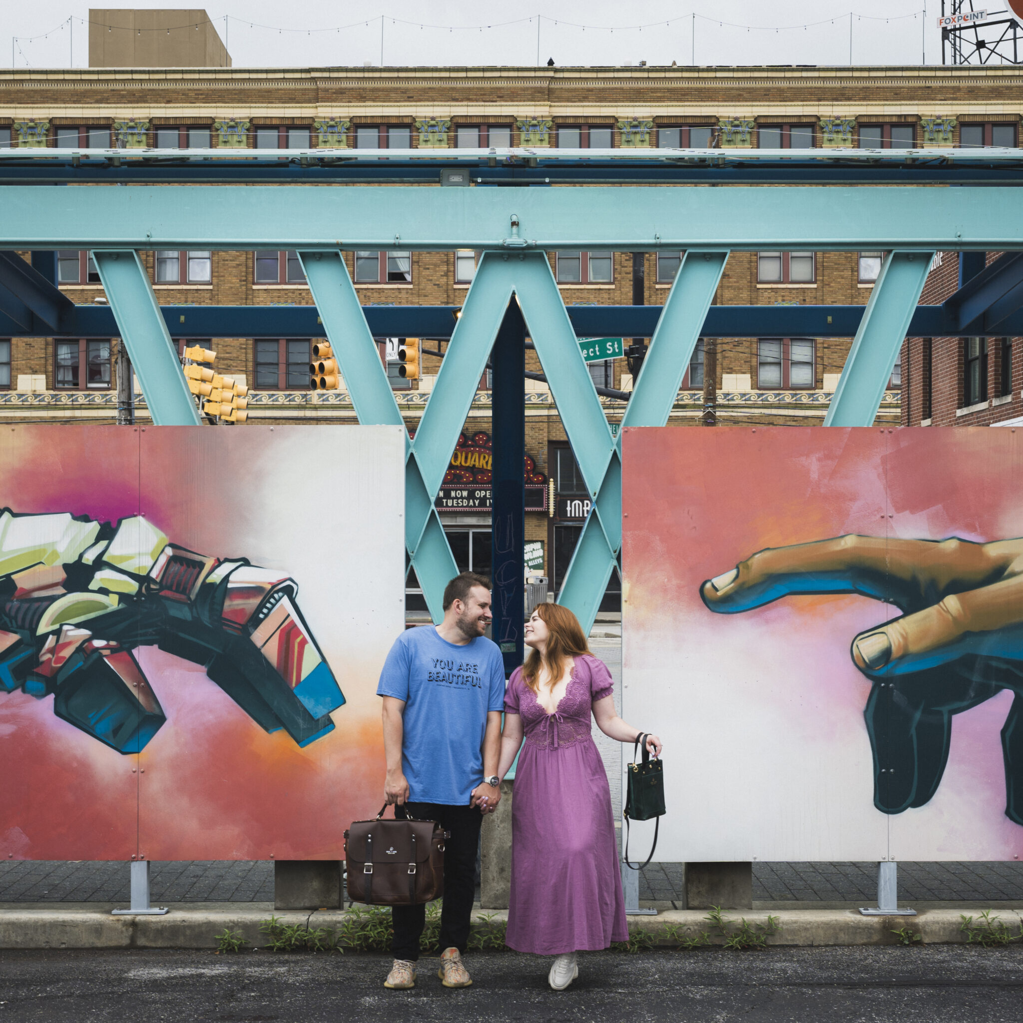 Couple holding hands and gazing lovingly at each other in front of a mural