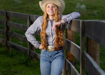 Red-headed girl dressed in western style apparel next to a rodeo gate
