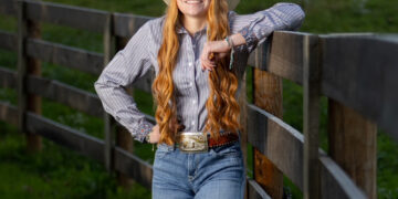 Red-headed girl dressed in western style apparel next to a rodeo gate