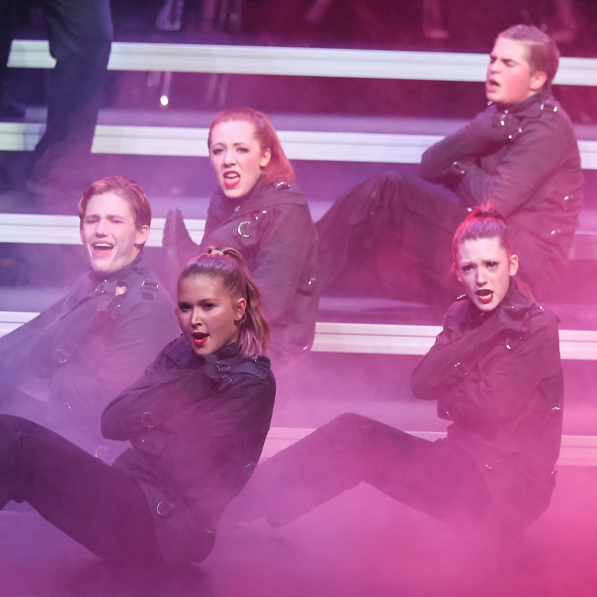 Choir members wearing biker gear and sitting on a floor