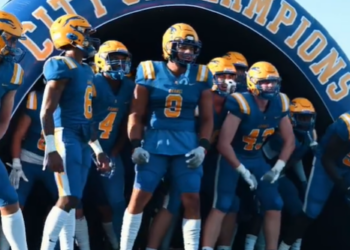 Football players in blue uniforms with yellow trim preparing to run onto a field