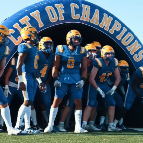 Football players in blue uniforms with yellow trim preparing to run onto a field