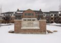 Holliday Farms Senior Living sign in front of a three-story brick apartment building, with snow covering the ground and overcast winter skies.