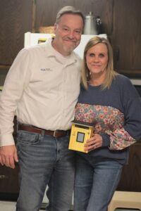Founders of the Feeding Team nonprofit pose with a miniature version of their signature yellow "no-questions-asked" outdoor food pantry.