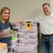 Founders of the Feeding Team nonprofit pose with stacks of donated beverages and a model of their "no-questions-asked" yellow food pantry.