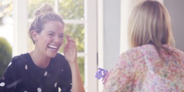 Two Female Friends In Coffee Shop Meeting Up In Socially Distanced Way Viewed Through Window