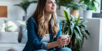 Shot of young woman drinking a cup of coffee while sitting on couch in living room at home.