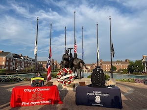 Memorial display in Carmel, Indiana, featuring fire and police department tables in front of the Carmel Clay Veterans Memorial bronze sculpture