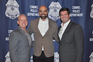 Three men posing at a Carmel Police Department event in front of a branded blue backdrop with police badge graphics.