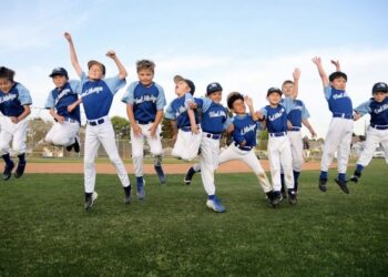 A joyful team of youth baseball players jumping together in celebration on an outdoor field