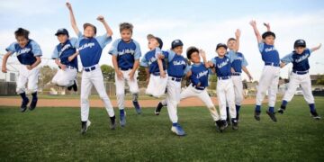 A joyful team of youth baseball players jumping together in celebration on an outdoor field