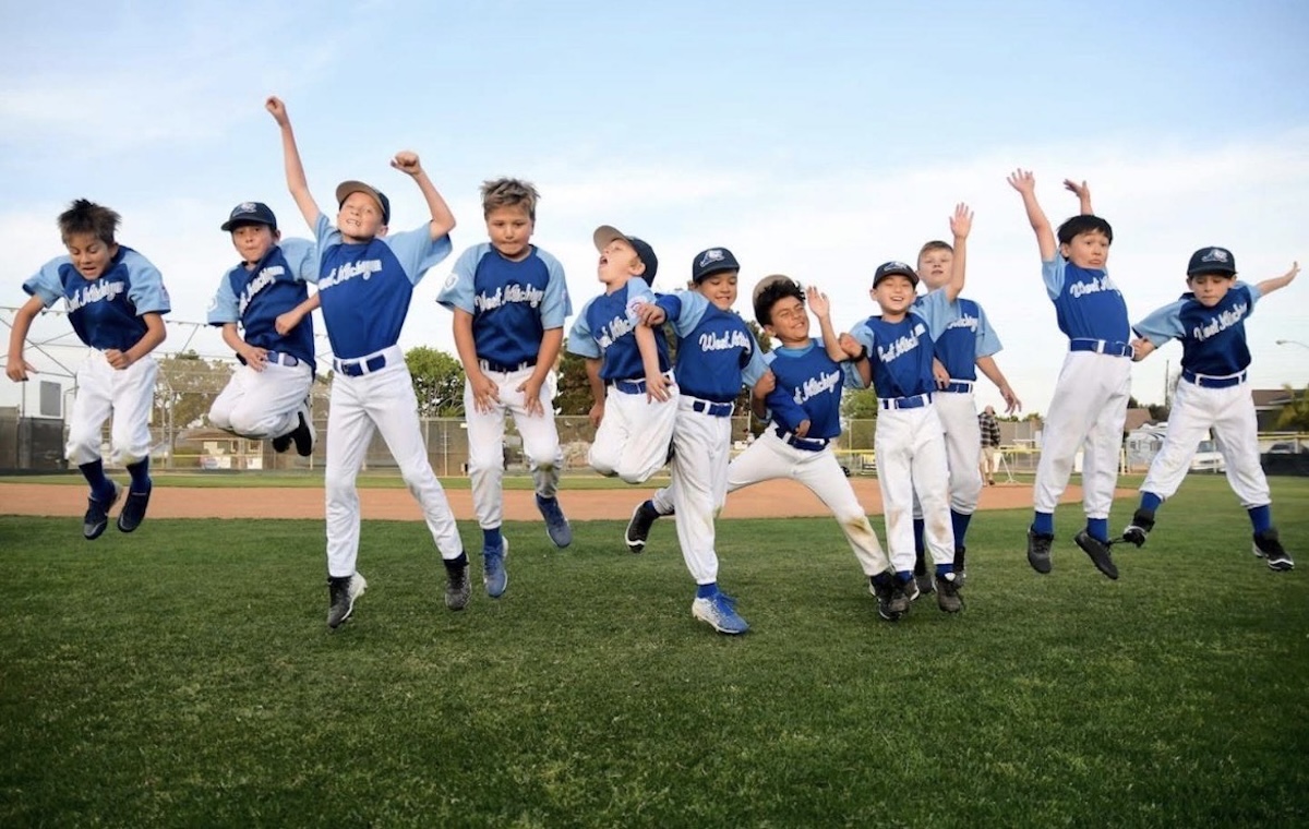 A joyful team of youth baseball players jumping together in celebration on an outdoor field