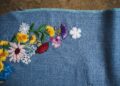 Multi-colored floral embroidery in a curved pattern on a textured blue fabric background.