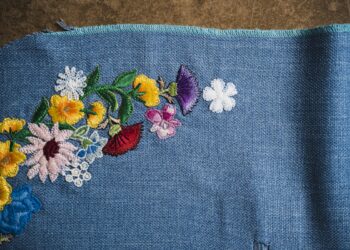 Multi-colored floral embroidery in a curved pattern on a textured blue fabric background.