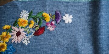 Multi-colored floral embroidery in a curved pattern on a textured blue fabric background.