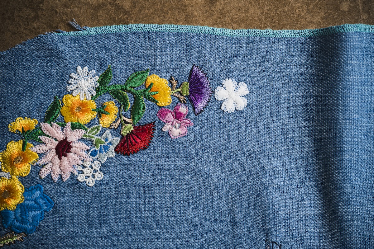 Multi-colored floral embroidery in a curved pattern on a textured blue fabric background.