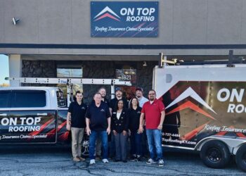 A team of eight employees from On Top Roofing stands together in front of their office building, flanked by a branded white pickup truck and a matching trailer.