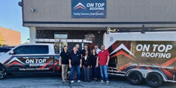 A team of eight employees from On Top Roofing stands together in front of their office building, flanked by a branded white pickup truck and a matching trailer.