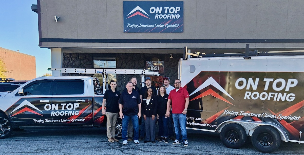 A team of eight employees from On Top Roofing stands together in front of their office building, flanked by a branded white pickup truck and a matching trailer.