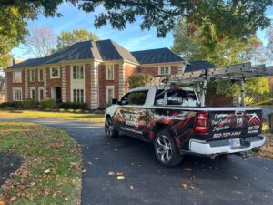 An On Top Roofing pickup truck, equipped with a ladder rack and branding, is parked on a paved driveway in front of a large, two-story brick house with a dark shingled roof.