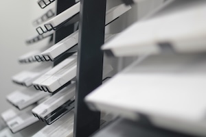 A close-up, shallow-depth-of-field shot of several white stone and tile samples arranged on a black vertical display rack in a showroom. The samples, likely marble, granite, or quartz, are rectangular and stacked at an angle, with the closest ones appearing softly blurred. The background is a clean, neutral white, emphasizing the textures and subtle variations of the stone materials.