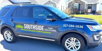A side profile of a dark blue Ford Explorer parked on a residential street in front of modern suburban homes. The front door of the SUV features a professional vinyl decal with the "Southside Turf Solutions" logo, which includes a stylized green grass graphic and the slogan "Because the grass CAN be greener." The company's phone number, 317-286-1636, is clearly displayed in white text on the front fender. The vehicle has chrome accents along the bottom and multi-spoke silver alloy wheels.