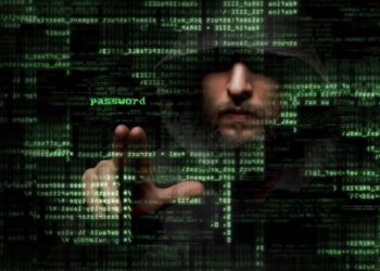 A hooded man's face is partially obscured by shadows and layers of glowing green computer code and symbols. The word "password" is highlighted in bright green near his hand, which is extended as if interacting with a digital interface. The dark, atmospheric image suggests themes of cybersecurity, hacking, or digital identity.