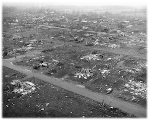 A historical black-and-white aerial photograph showing the catastrophic devastation in the Sunnyside subdivision of Dunlap, Indiana, following the F4 tornado of the 1965 Palm Sunday outbreak. The image reveals a landscape of flattened homes and scattered debris, with a single road cutting through the ruins as far as the eye can see.
