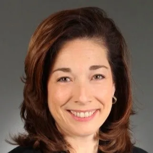 A professional headshot of Melissa Stapleton Barnes, a corporate executive and ethics leader. She is smiling warmly with medium-length brown hair, wearing a dark top against a neutral gray background.