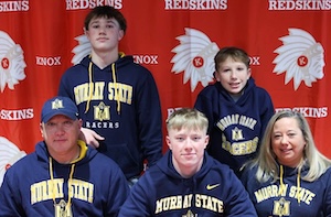 A family poses for a celebratory photo on National Signing Day in front of a red Knox High School Redskins backdrop. Myles McLaughlin, a record-setting running back, sits centrally in a navy blue Murray State Racers hoodie, joined by four family members also wearing matching Murray State apparel. The group is smiling, commemorating his commitment to play Division I football.