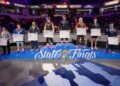 A wide shot of the 190-pound weight class podium at the 2026 IHSAA Boys Wrestling State Finals inside Gainbridge Fieldhouse in Indianapolis. Eight state-placing wrestlers stand on a multi-tiered blue podium decorated with the "IHSAA State Finals" logo. The state champion, Michael White of Lawrence North (undefeated at 47-0), stands on the highest central tier wearing a gold medal. Other place-winners stand to his sides, each holding a large white bracket sheet and wearing their respective medals. The background shows the brightly lit arena with spectators in the stands and various corporate sponsor banners for Salesforce, IndyStar, and FanDuel.