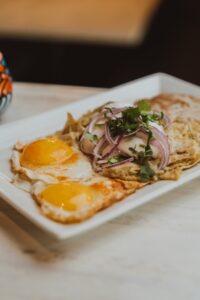 Authentic Mexican breakfast chilaquiles served on a white rectangular plate, featuring crispy tortilla chips simmered in salsa and garnished with pickled onions and eggs.