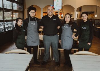 A professional group portrait of five employees at a Toro Mexican restaurant, standing between tables in a clean, contemporary setting.