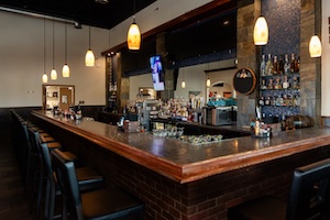 The interior of a contemporary restaurant bar featuring a brick base, a polished countertop, and a fully stocked back bar with various spirits and glassware.