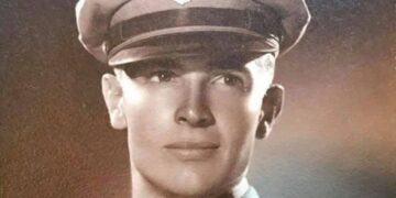 A classic military studio portrait of a clean-shaven young soldier wearing a service cap with a prominent eagle crest, reflecting World War II-era style.