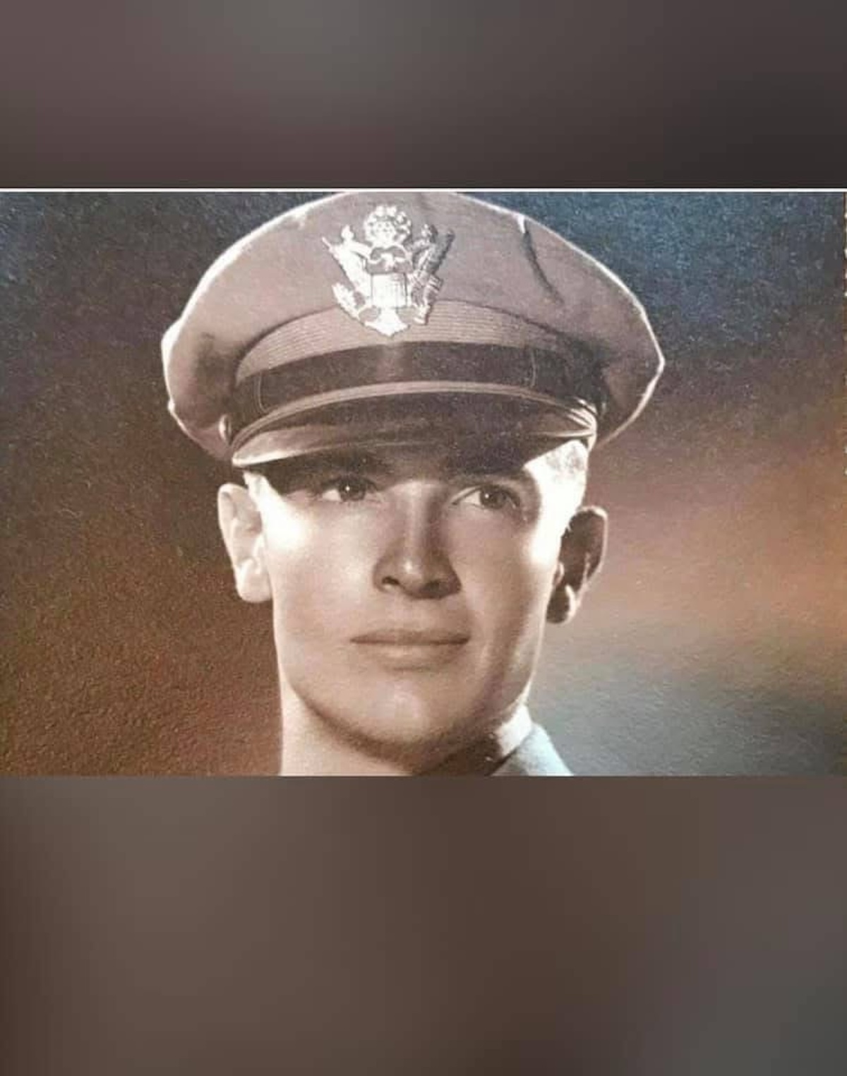 A classic military studio portrait of a clean-shaven young soldier wearing a service cap with a prominent eagle crest, reflecting World War II-era style.
