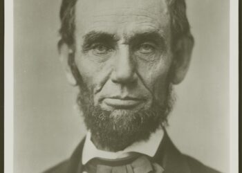 A detailed, head-and-shoulders black-and-white portrait of a beardless Abraham Lincoln, photographed by Alexander Hesler in Springfield, Illinois, on June 3, 1860. Lincoln is facing slightly right, with a thoughtful and calm expression. He has dark, somewhat tousled hair, deep-set eyes, and visible lines etched into his face. He is wearing a dark suit jacket, a white collared shirt, and a dark, slightly askew bowtie. The background is a plain, light grey tone.