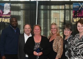 A group of six colleagues stand smiling together in front of a black curtain backdrop at an awards event. A woman in the center holds a glass trophy award. Behind them, large banners read "Best Places to Work in Indiana 2026", "Presented by KSM CPAs & Advisors", and "Walk of Fame" with the hashtag #BPTWIN.