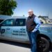 A man stands on a paved driveway next to a light blue Ford Maverick pickup truck with commercial vehicle graphics. The side of the truck displays a "PS PREMIER SHADE" logo and the text "YOUR LOCAL SHADE EXPERT." The truck bed features text reading "Retractable Awnings, Retractable Screens," the phone number (260) 255-6004, and a large QR code.