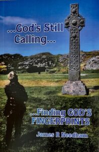 The book cover for "...God's Still Calling... ...Finding GOD'S FINGERPRINTS" by James R Needham. The background features an outdoor landscape on a sunny day with a green grassy field and rocky hills under a blue sky. On the right stands a tall, ancient stone Celtic high cross covered in detailed carvings. On the lower left, a person is seen from behind, standing in shadow and looking toward the cross. The book title and author's name are printed in white text with blue outlines.