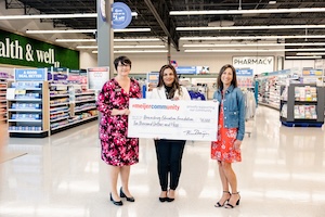 Three women smile while standing inside the health and wellness aisle of the newly opened Meijer Supercenter in Brownsburg, Indiana. They are holding a large ceremonial presentation check from "Meijer Community" made out to the "Brownsburg Education Foundation" for the amount of ten thousand dollars ($10,000). The background showcases bright grocery store lighting, product shelves, and a large green wall sign that reads "health & well" alongside a "PHARMACY" sign.