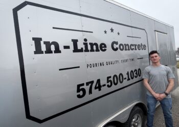 A man in a grey t-shirt and jeans stands next to a large silver commercial trailer. The trailer features a prominent black logo reading "In-Line Concrete" with the slogan "POURING QUALITY, EVERY TIME" and the phone number 574-500-1030 printed in large black font.