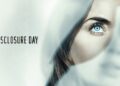 A cinematic movie poster features the title "DISCLOSURE DAY" in a clean, black, sans-serif font on the left against a bright white background. The right side shows a close-up, dramatic composite image of a woman's face partially obscured by layered, translucent white fabric. Her intense, bright blue eye is fully visible and in sharp focus, while her hair sweeps across her cheek and a faded, secondary image of her face appears in the soft-focus background.