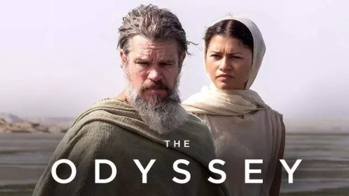 A movie-style promotional image titled "THE ODYSSEY" featuring actors Matt Damon and Zendaya in historical, desert-style clothing. Matt Damon stands in the foreground with a long, graying beard and a draped green cloak. Zendaya stands slightly behind him to the right, looking forward with a serious expression while wearing a cream-colored garment and head wrap. The background is a vast, hazy desert landscape.
