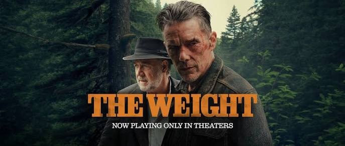 Poster for the movie "The Weight" showing Ethan Hawke and Russell Crowe. The foreground features a rugged, serious-looking Ethan Hawke with short, graying hair and dynamic facial features. Slightly behind him to the left stands Russell Crowe, wearing a dark fedora hat and a matching jacket over a button-up shirt, looking off to the side. They are positioned against a dense, dark green pine forest backdrop. The title "THE WEIGHT" is prominently displayed across the bottom in large, bold orange block letters, with the tagline "NOW PLAYING ONLY IN THEERS" written underneath in smaller white text.