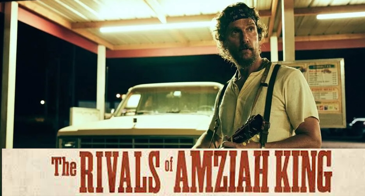 A close-up shot of actor Matthew McConaughey in the film "The Rivals of Amziah King." He stands under a brightly lit carport at night, looking off-camera with a serious expression. He has longer curly hair, a beard, and wears a blue bandana, a light yellow t-shirt, and dark suspenders with a rifle strapped to his chest. A vintage white pickup truck sits in the background under the fluorescent lights.