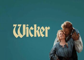 • Promotional poster for "Wicker" against a solid teal background. On the right, an older woman with blonde hair wearing a blue, textured rustic dress leans back smiling with her eyes closed. She is being embraced from behind by a creature or man whose face, head, and hands appear completely woven out of wicker or straw. The stylized text "Wicker" is written in a cream-colored, vintage serif font on the left.