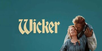 • Promotional poster for "Wicker" against a solid teal background. On the right, an older woman with blonde hair wearing a blue, textured rustic dress leans back smiling with her eyes closed. She is being embraced from behind by a creature or man whose face, head, and hands appear completely woven out of wicker or straw. The stylized text "Wicker" is written in a cream-colored, vintage serif font on the left.