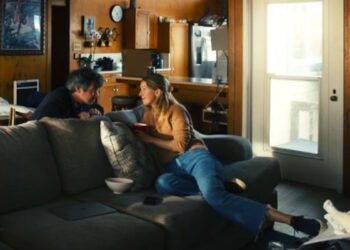 Director Nathan Fielder (left) and former Theranos CEO Elizabeth Holmes (center) captured in a candid, high-contrast shot inside a kitchen from the film 'You Can See Everything'.